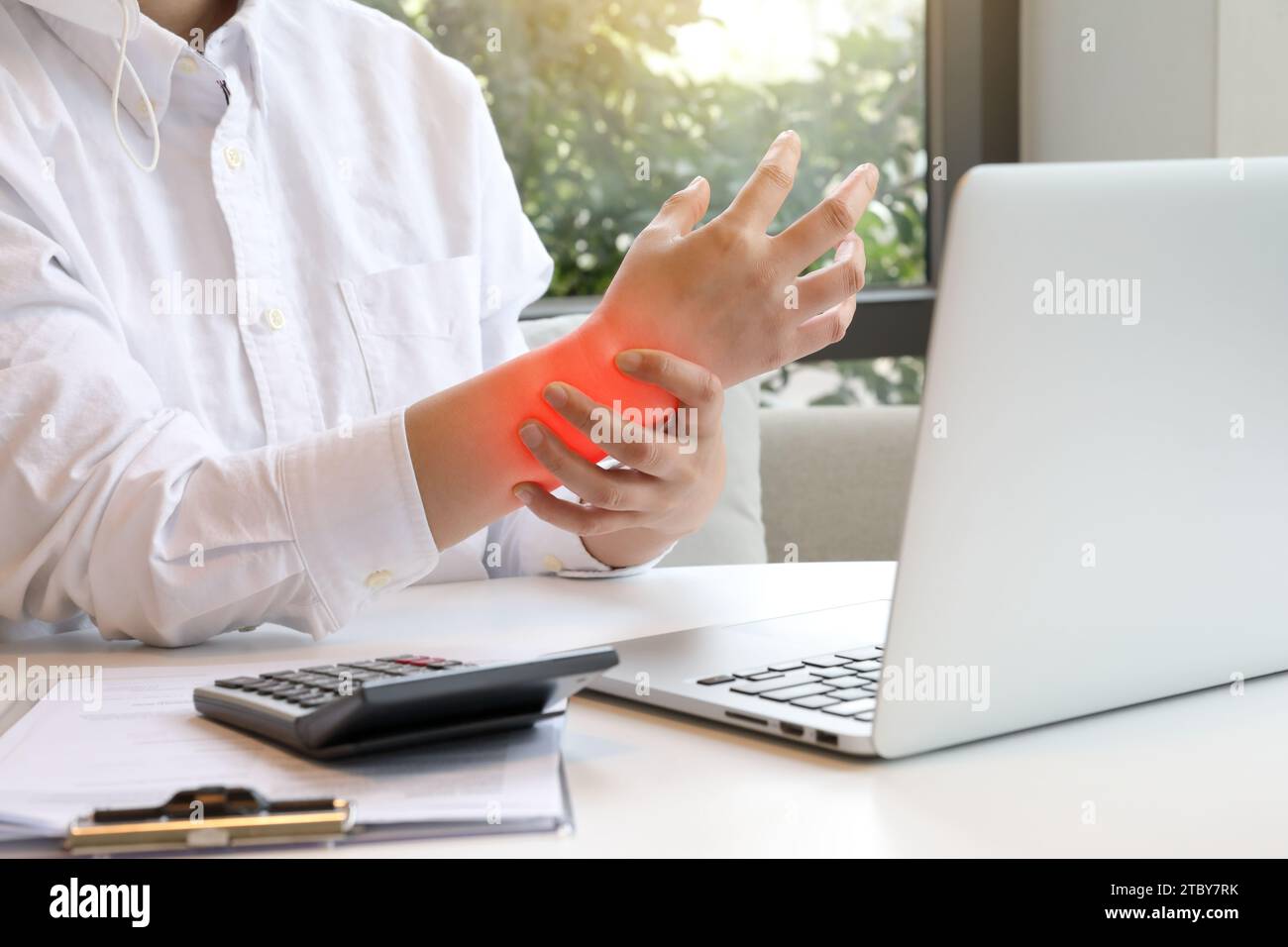 Woman typing on laptop is holding her sore wrist with carpal tunnel