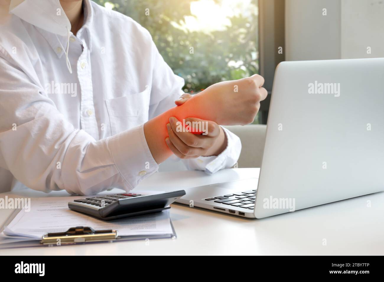 Woman typing on laptop is holding her sore wrist with carpal tunnel
