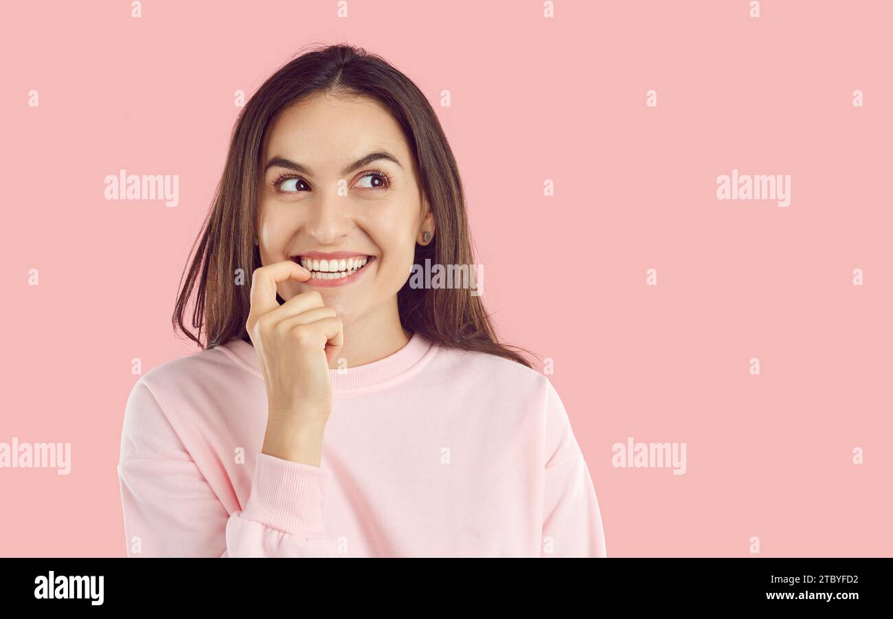 Happy woman standing on pink background, looking to copy space side, thinking and smiling Stock Photo
