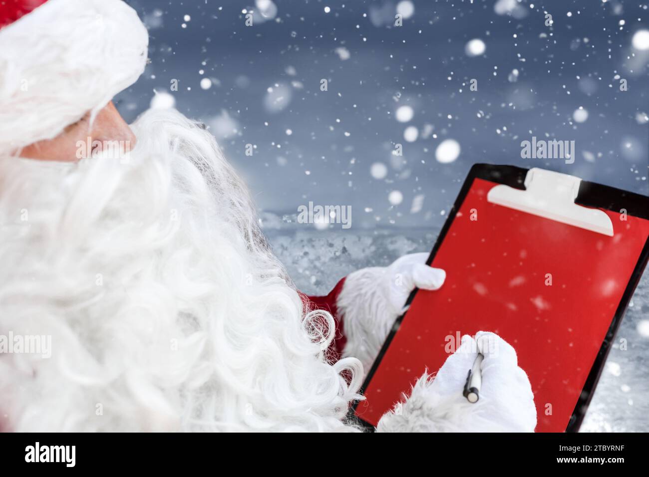 Close-up portrait of a young Santa Claus writing notes on the red paper Stock Photo