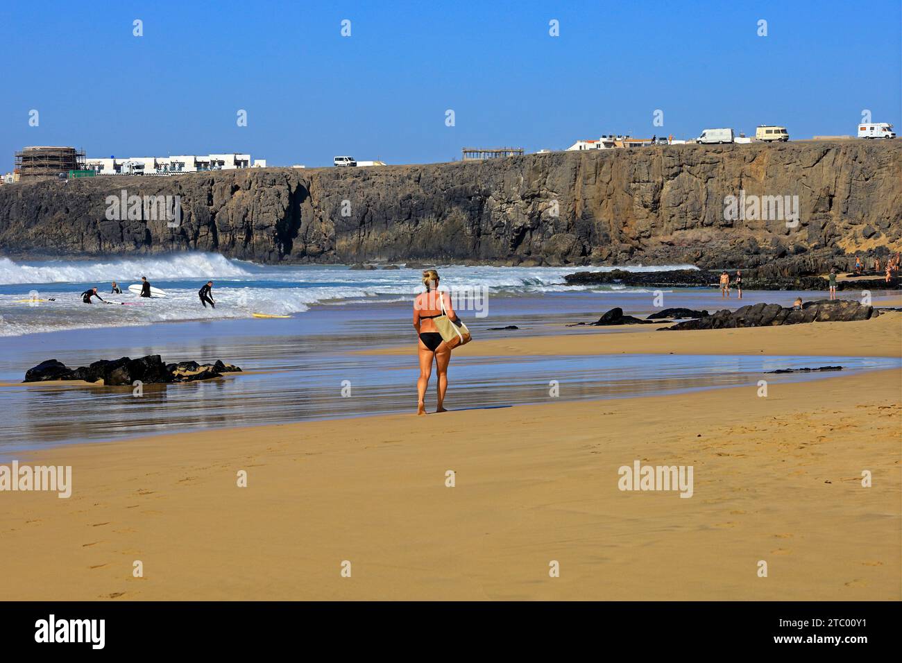 Blond woman in a swimsuit walking along the surfing beach at El Cotillo