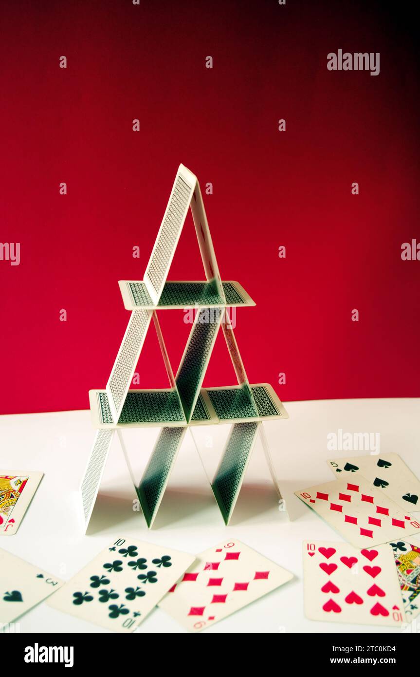 Playing card pyramid in balance, made with poker cards on a red background and scattered cards Stock Photo