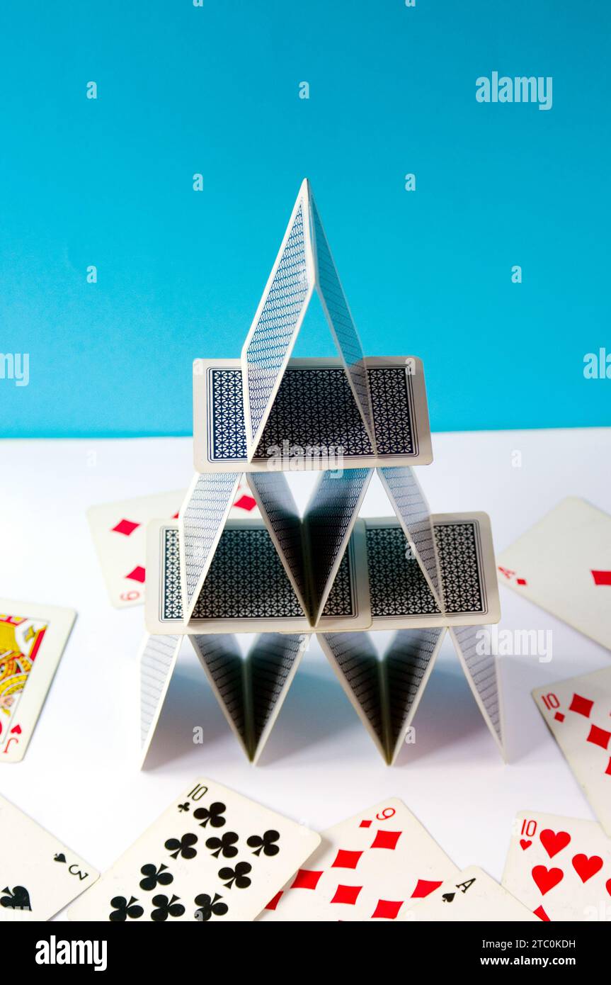 Playing card pyramid in balance, made with poker cards on a blue background and scattered cards. Stock Photo