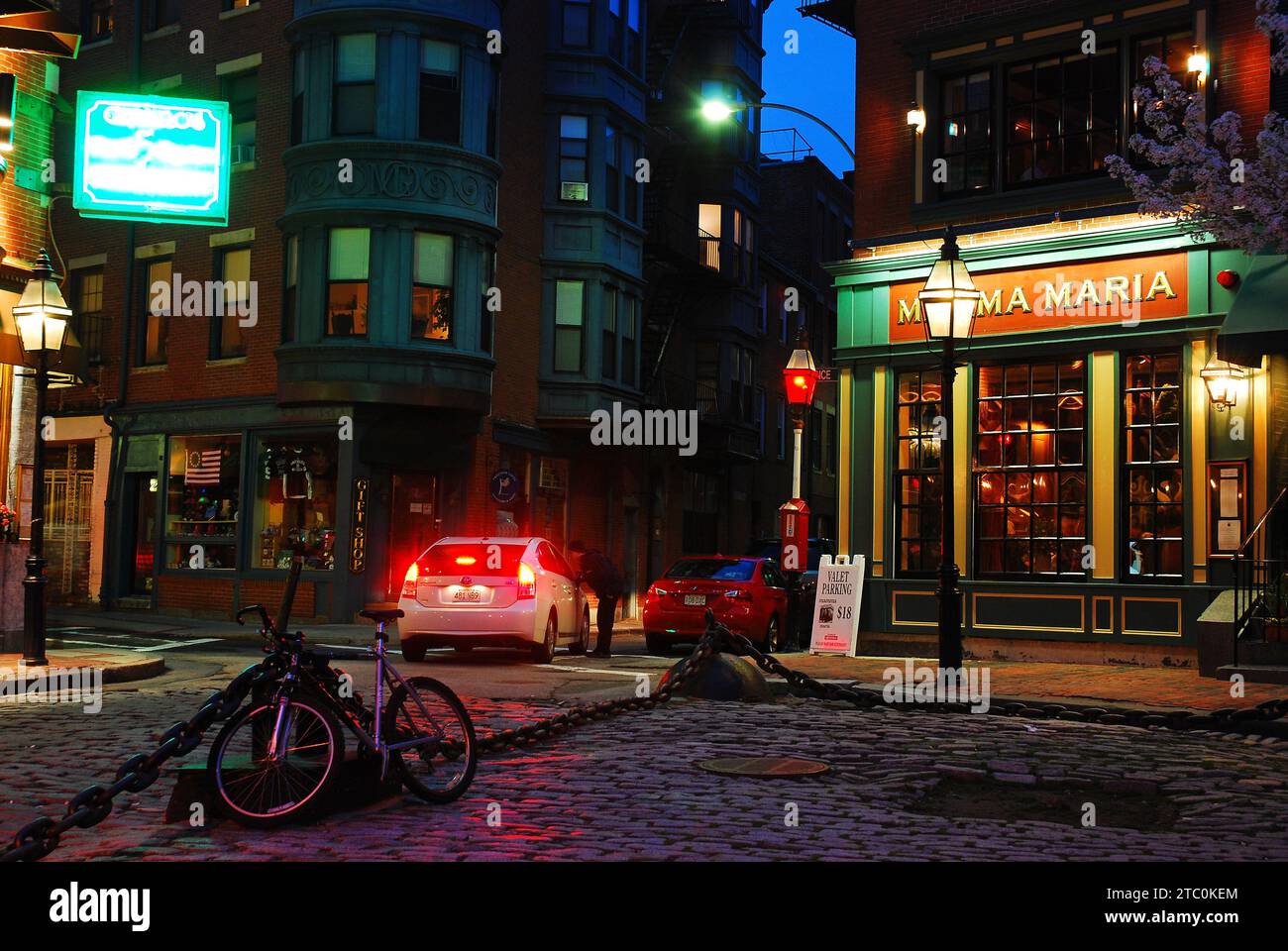 A bike is chained to a larger chain, surrounded by Italian restaurants and cafes in the North End district of Boston Stock Photo