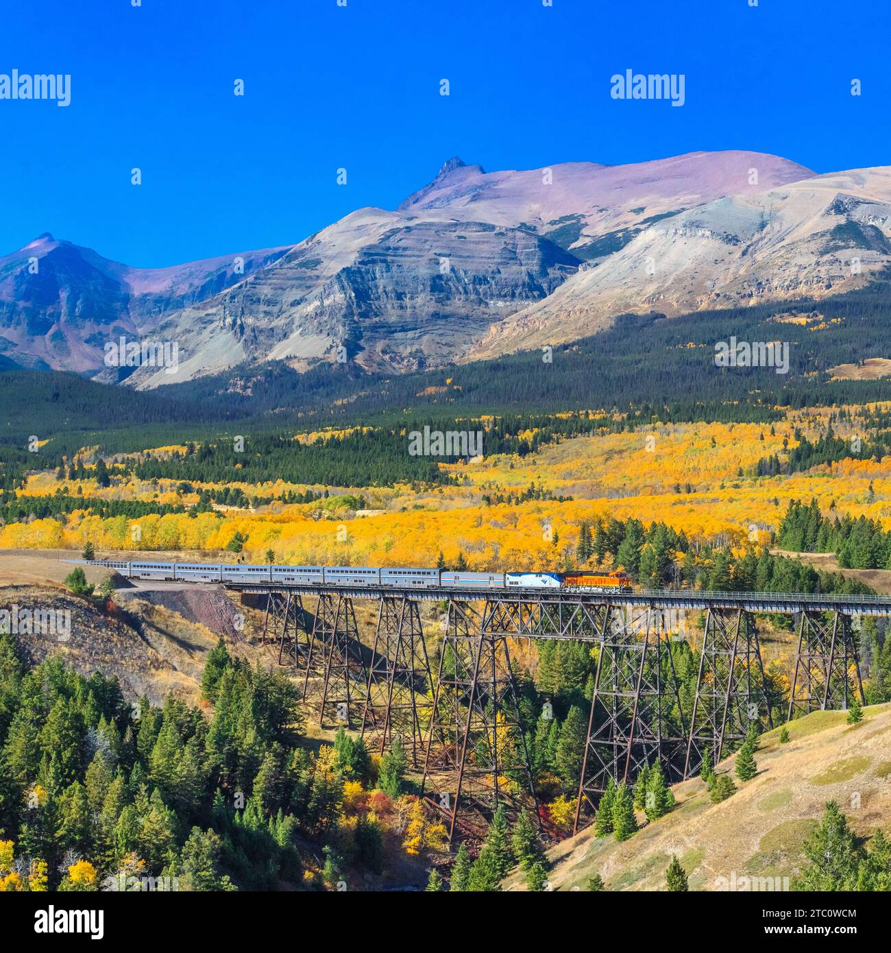 passenger train crossing over a trestle in autumn below peaks of