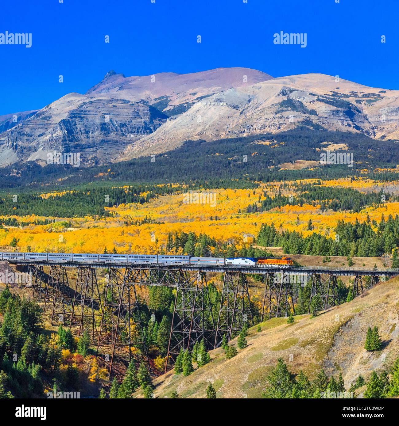 passenger train crossing over a trestle in autumn below peaks of
