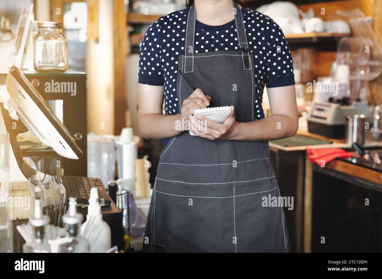 a woman coffee shop in apron is holding memo ready to take order in front of counter. Stock Photo