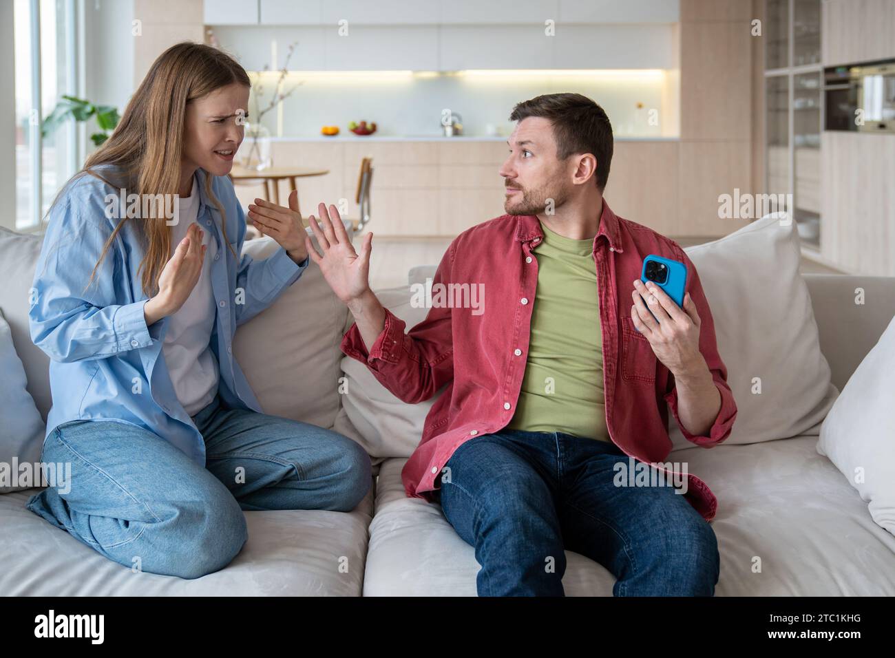 Sly husband cheater hiding smartphone display from unhappy nervous reproachful wife during quarrel Stock Photo