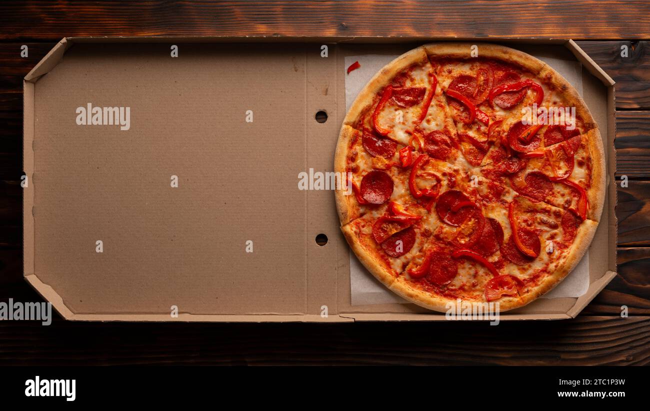 Pepperoni pizza with bell peppers in open carton box on dark wooden table flat lay with copy-space Stock Photo