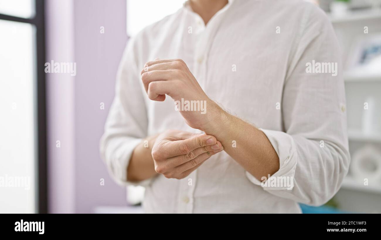 Caucasian man grimacing, suffering from searing wrist pain, standing alone in his quaint living room, depicts real struggle endured at home with hand Stock Photo