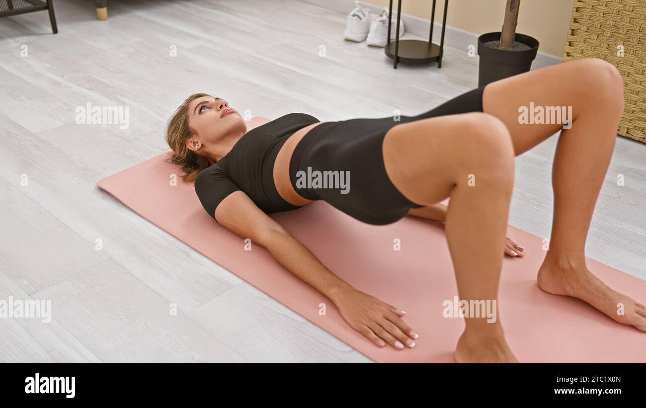 Young slim woman with blonde hair sitting on the yoga mat and doing  stretching exercises - pulls the leg to the body Stock Photo by  ©barselona_dreams 292992378