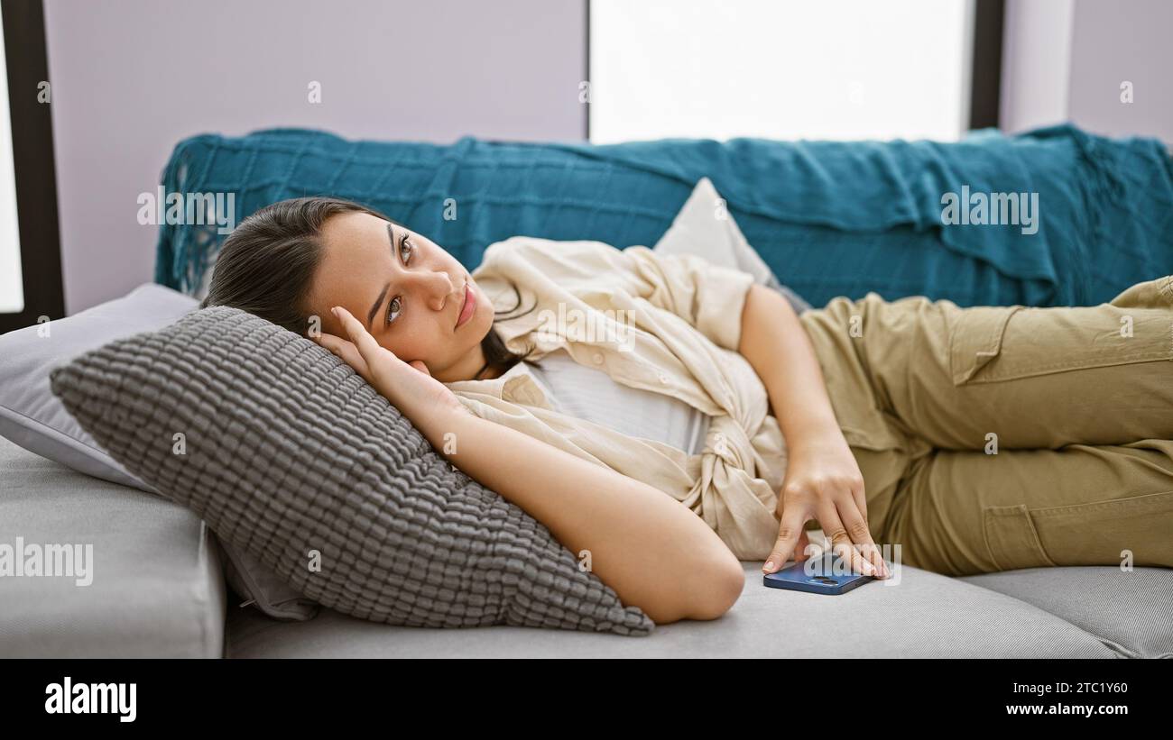 Unhappy young hispanic woman lying on the sofa at home, deeply ...
