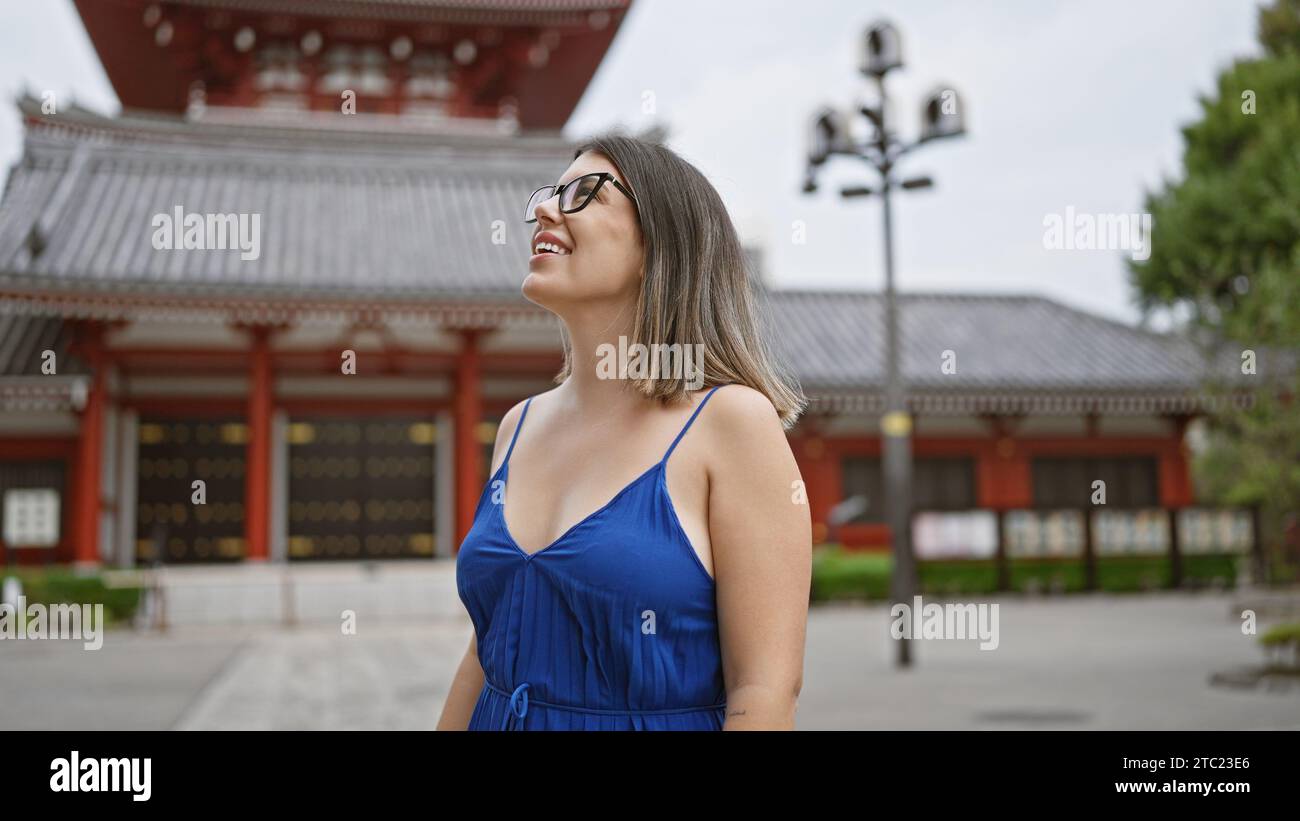 Cheerful, beautiful hispanic woman with glasses joyfully exploring and admiring the majestic senso-ji temple as she casually strolls, looking around w Stock Photo