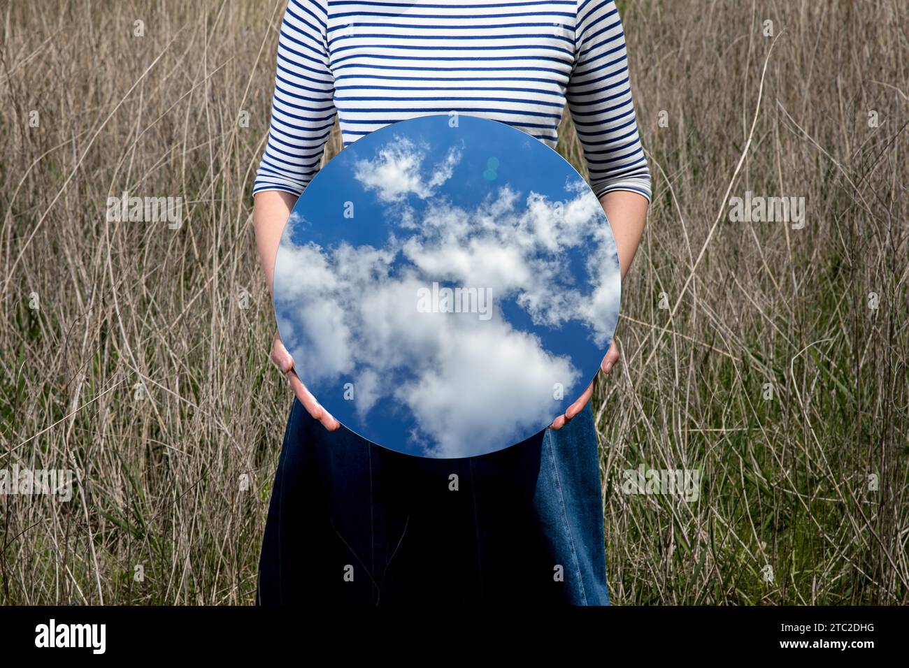 Surrealism with a woman holding a mirror and covering her face in the field with a transparent background behind the mirror Stock Photo