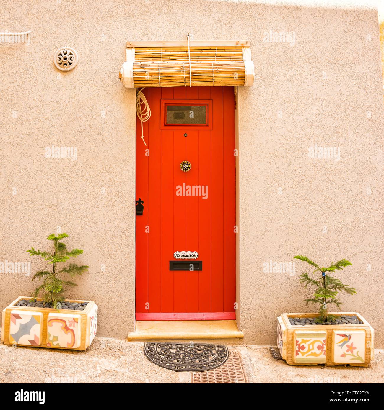 The Typical red door in Maltese villages with rolled up bamboo curtain cover Stock Photo