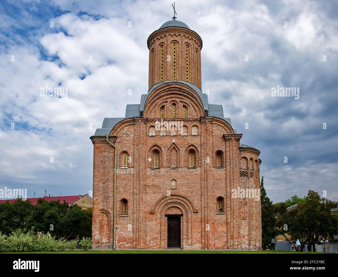 The Pyatnitskaya Church in Chernigov, Ukraine, a striking red brick building with a towering spire, is set against a picturesque backdrop of lush gree Stock Photo