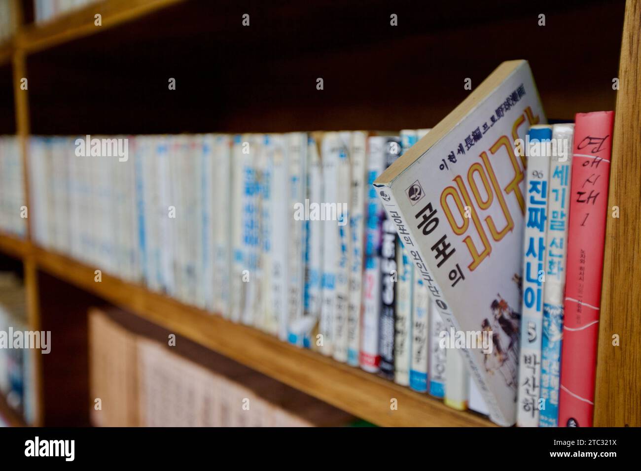 A single old Korean novel angles outwards from a neatly lined bookshelf, standing out as a symbol of literary history amidst orderly rows. Stock Photo