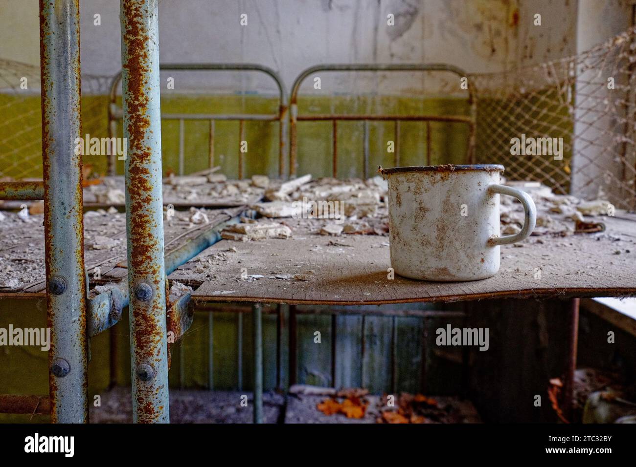 A white mug with a rusted rim and handle on a table. A white metal mug on a bed in an abandoned building in Chernobyl. Stock Photo
