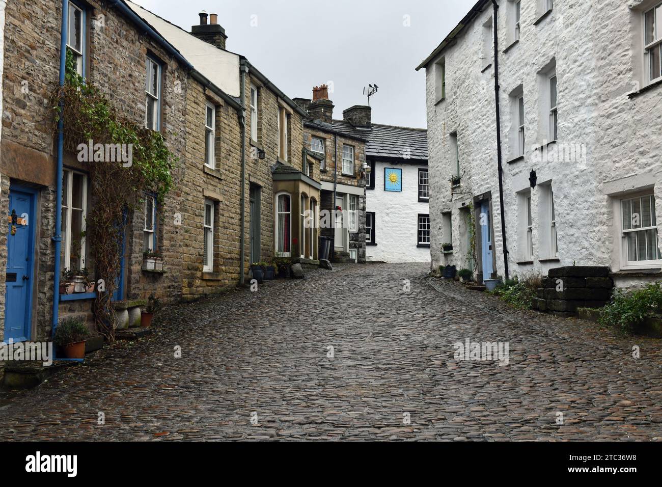 The cobbled main street through Dent village in Dentdale  - in the distance is the Sun Inn with cobbled streets and old houses in the centre Stock Photo