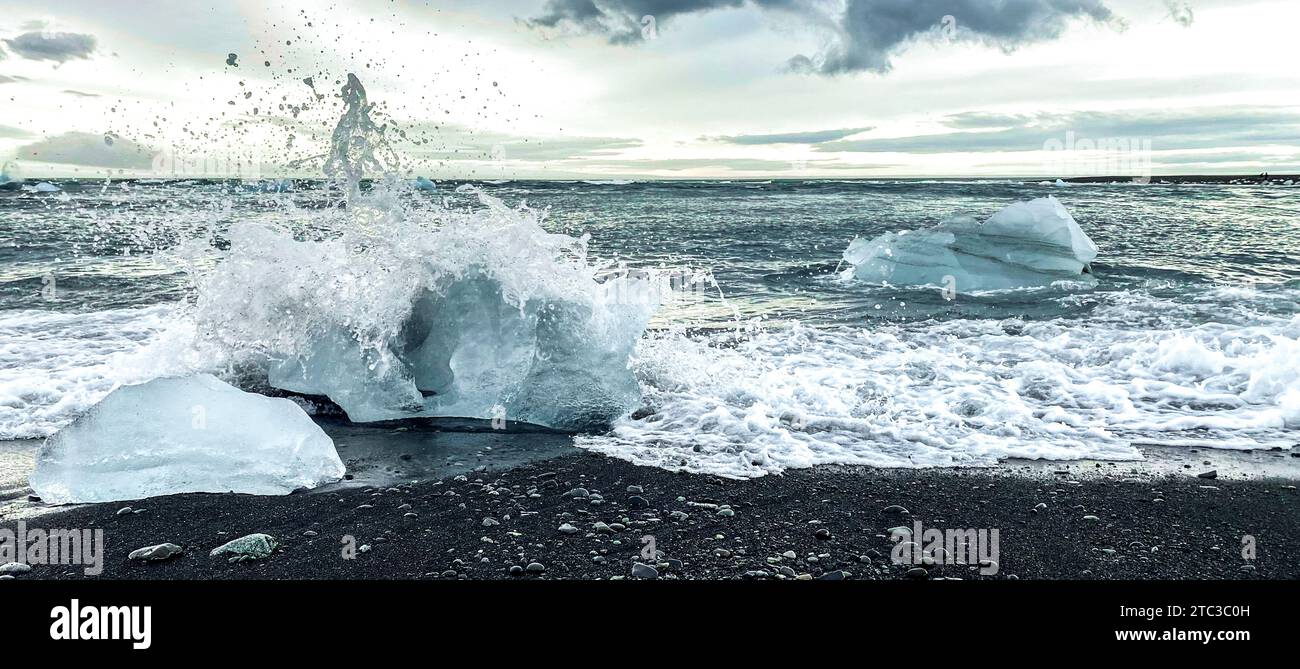 Wave Splashing Against Ice Chunk on Black Sand Beach in Iceland Stock Photo