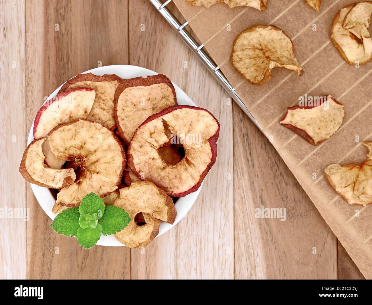 Dried apple rings in white bowl on a wooden table, homemade apple rings on a baking tray from the oven Stock Photo