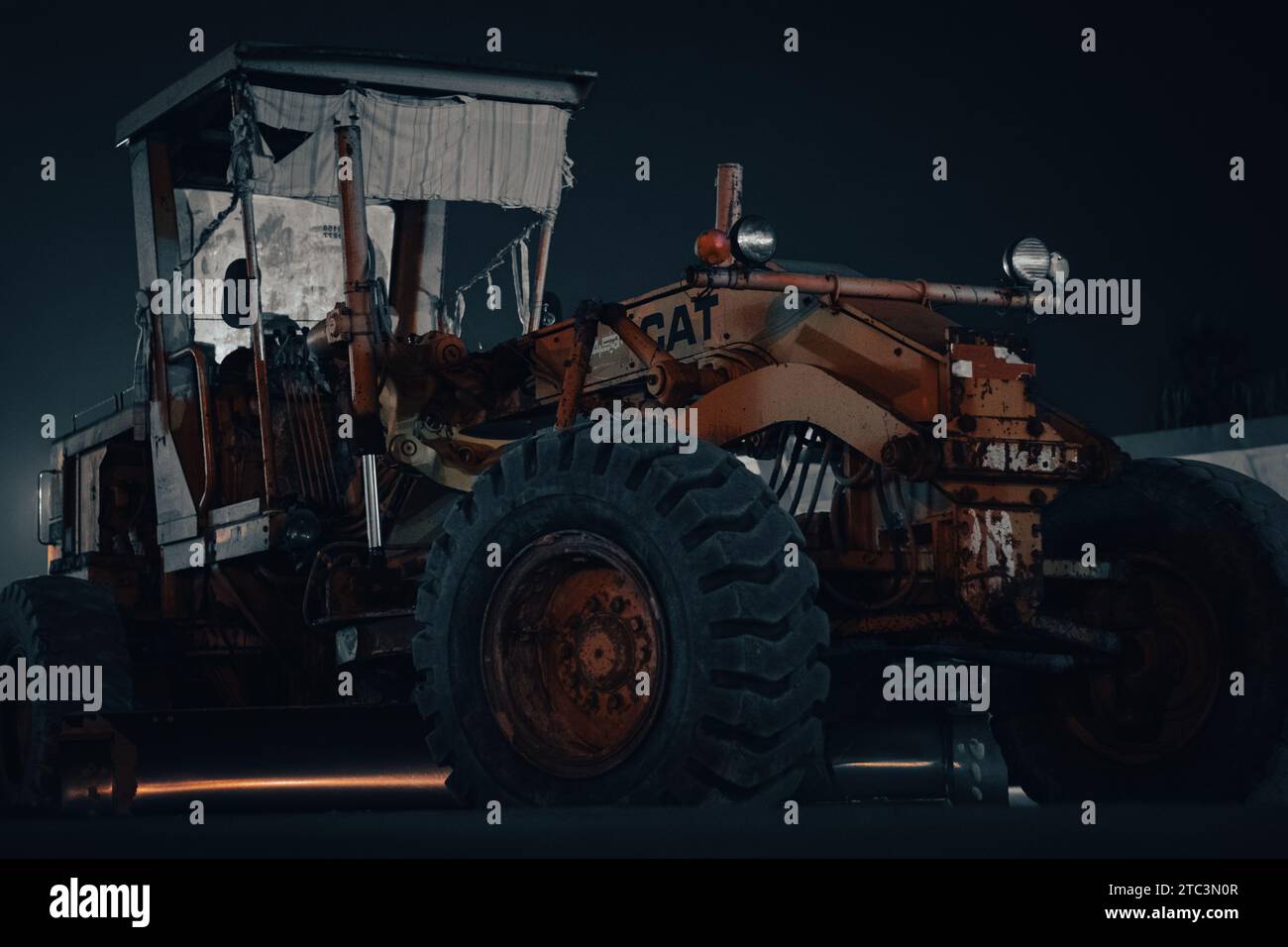 A tractor with a cab illuminated by the night sky driving along a paved