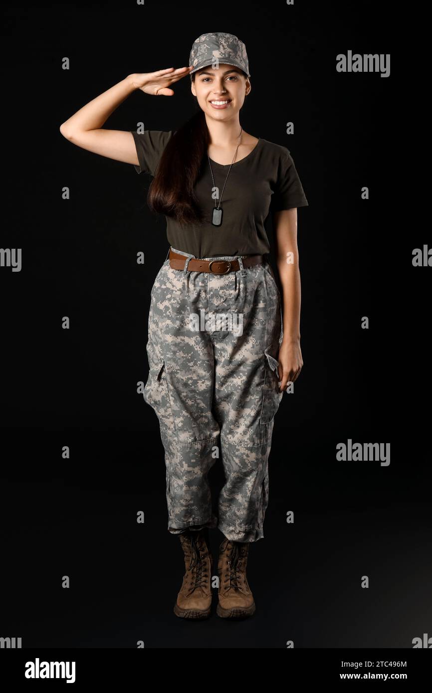 Confident young woman in military uniform saluting on black background ...