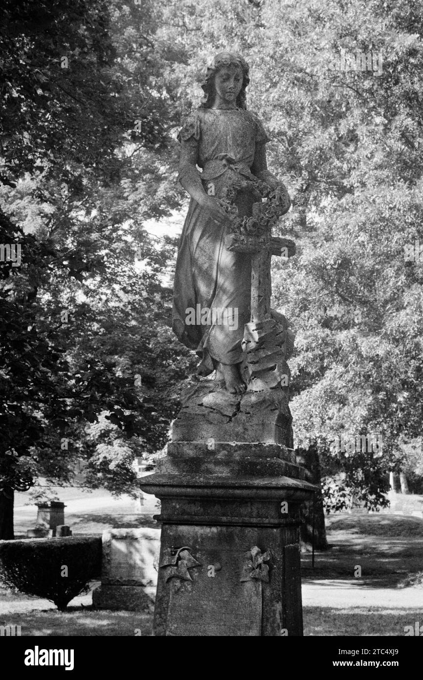 Lowell, Massachusetts - A large vintage monument of a woman standing with a cross and a wreath above the cemetery with brightly light foliage in the b Stock Photo