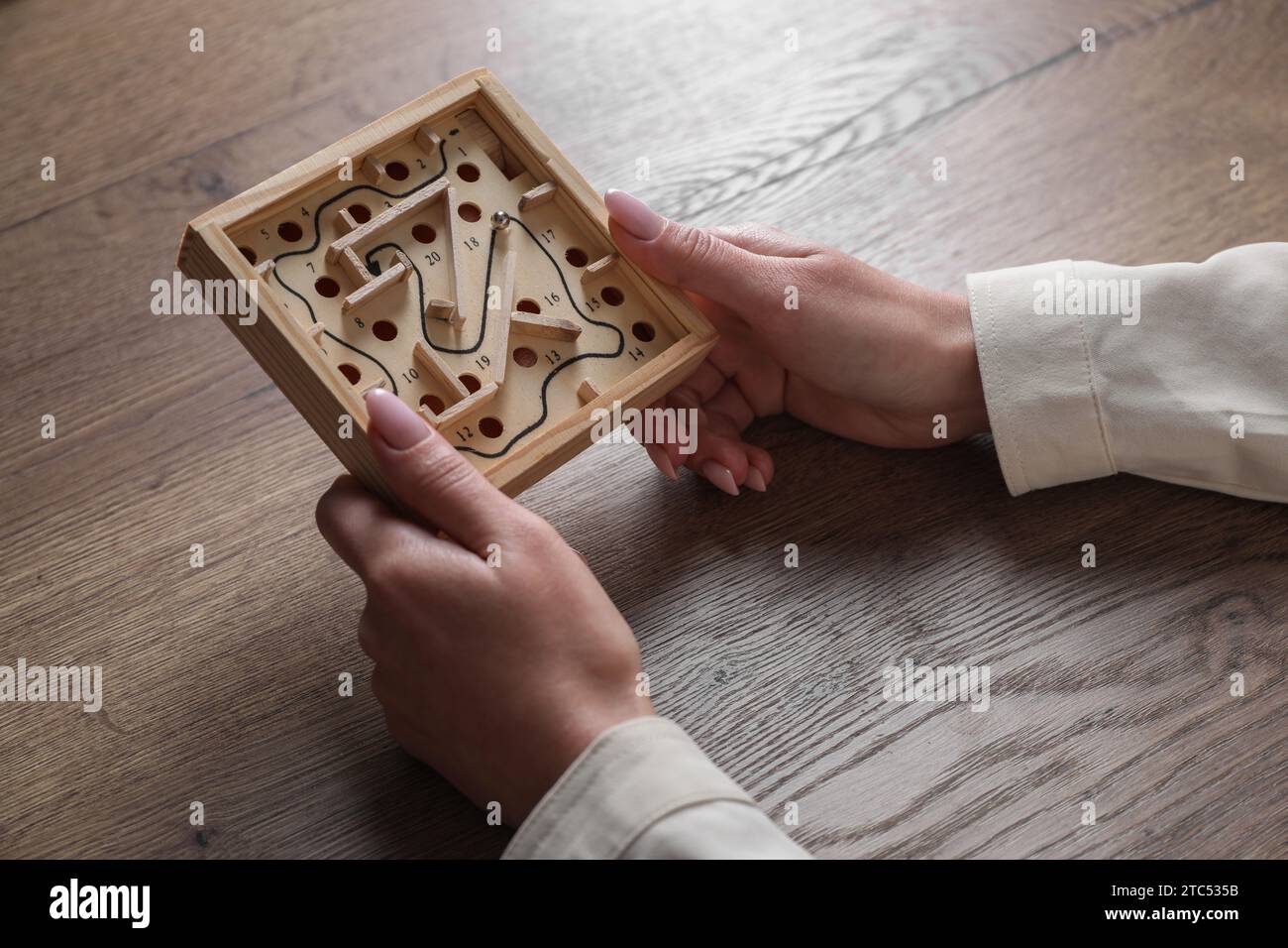 Woman holding wooden toy maze with metal ball at table, closeup Stock Photo