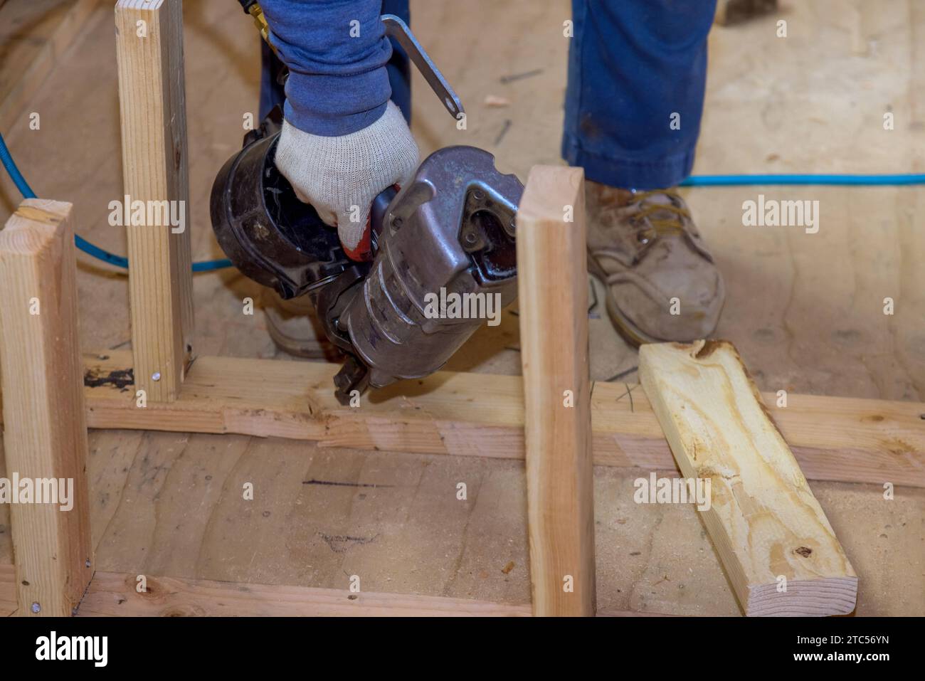 Builder uses an air hammer to nail wooden beams for support of building ...