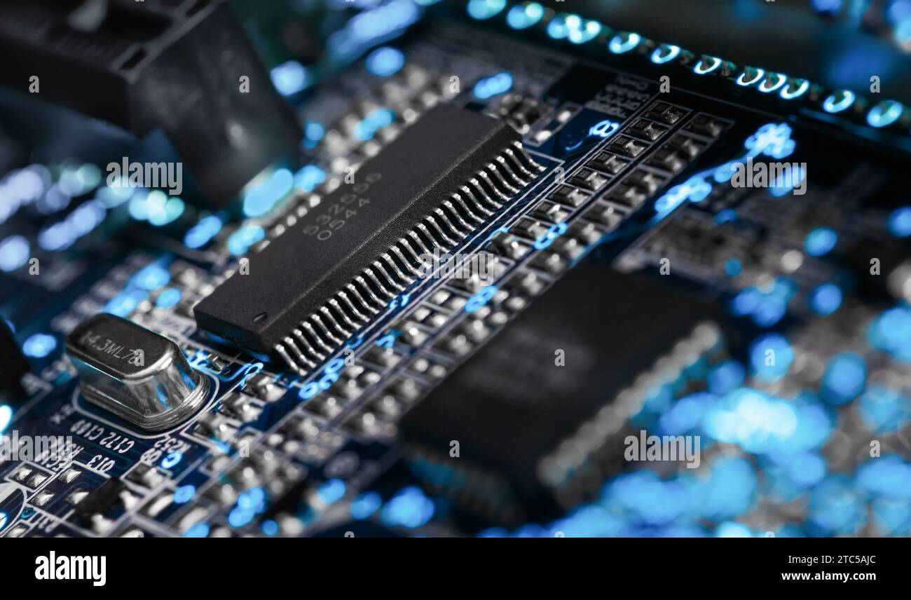 A microprocessor on a printed circuit board surrounded by auxiliary elements, backlit through the board. Macrofto in dark colors Stock Photo