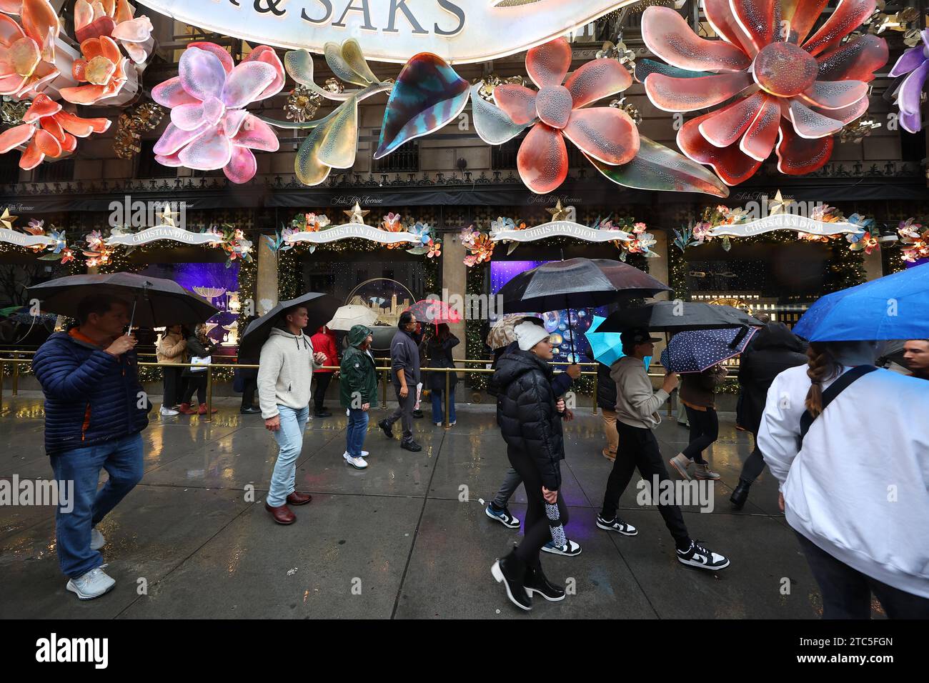 New York City, United States. 10th Dec, 2023. People are taking photos with mobile devices outside Saks Fifth Avenue while others are walking by in a light rain in New York, New York, on December 10, 2023. (Photo by Gordon Donovan/NurPhoto) Credit: NurPhoto SRL/Alamy Live News Stock Photo