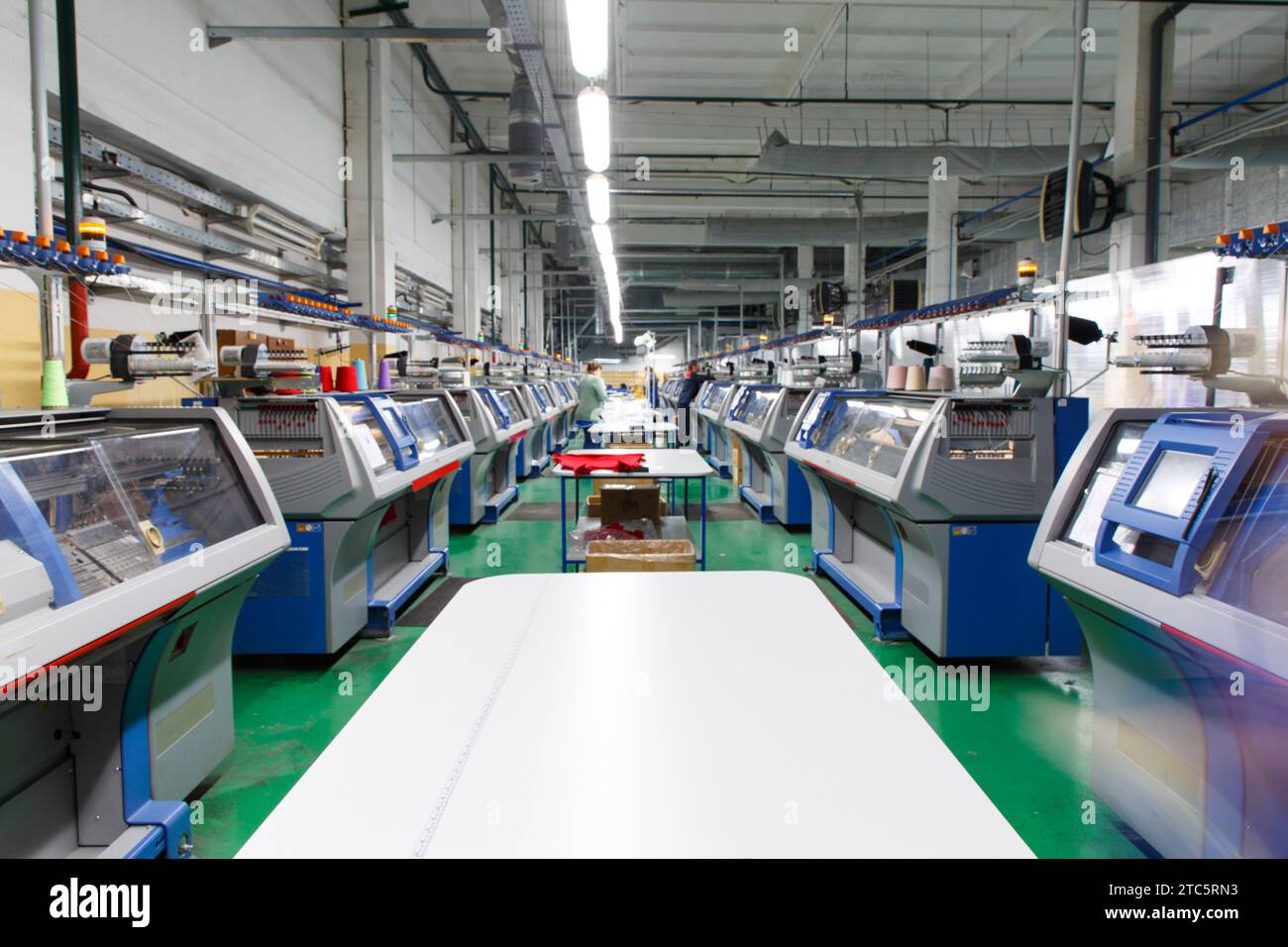 A row of industrial textil flat knitting machines in a knitwear factory. An industrial line of modern automatic knitting machines arranged in two rows Stock Photo