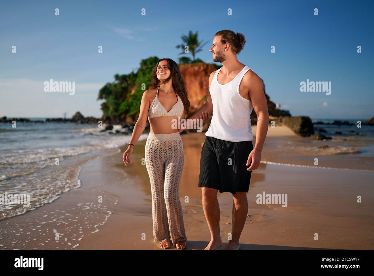 Romantic couple strolls on beach at sunset. Young man, woman walk hand ...