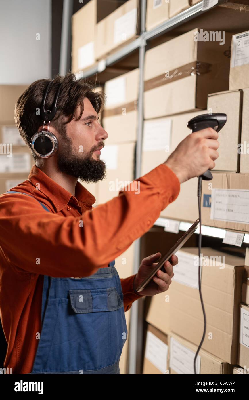 Warehouse worker in wireless headset scanning barcodes on boxes in a large warehouse Stock Photo