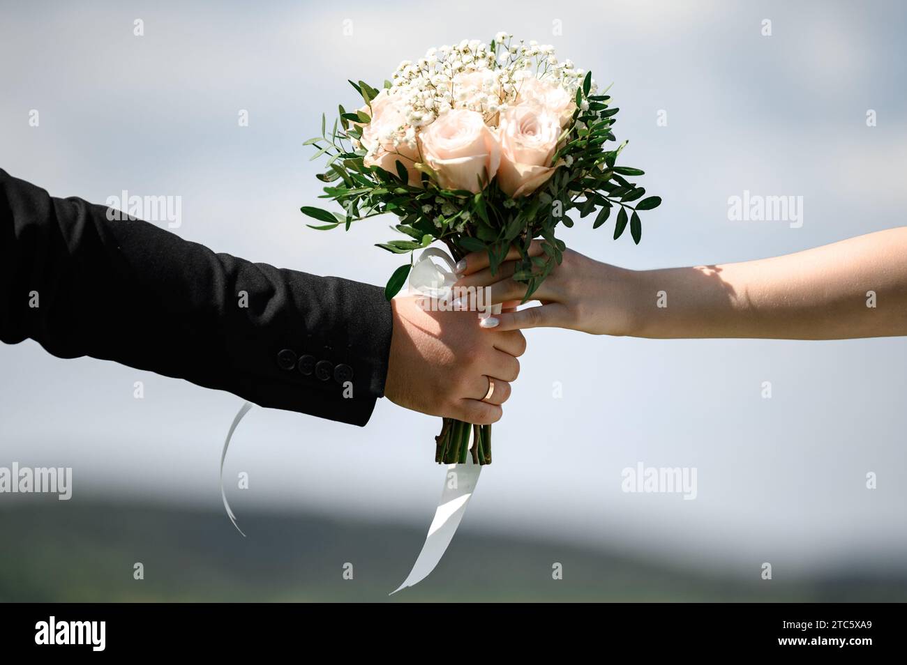 Bouquet for the bride in the hands of the grooms close-up on the background of the sky, fresh flowers for the bouquet. Stock Photo