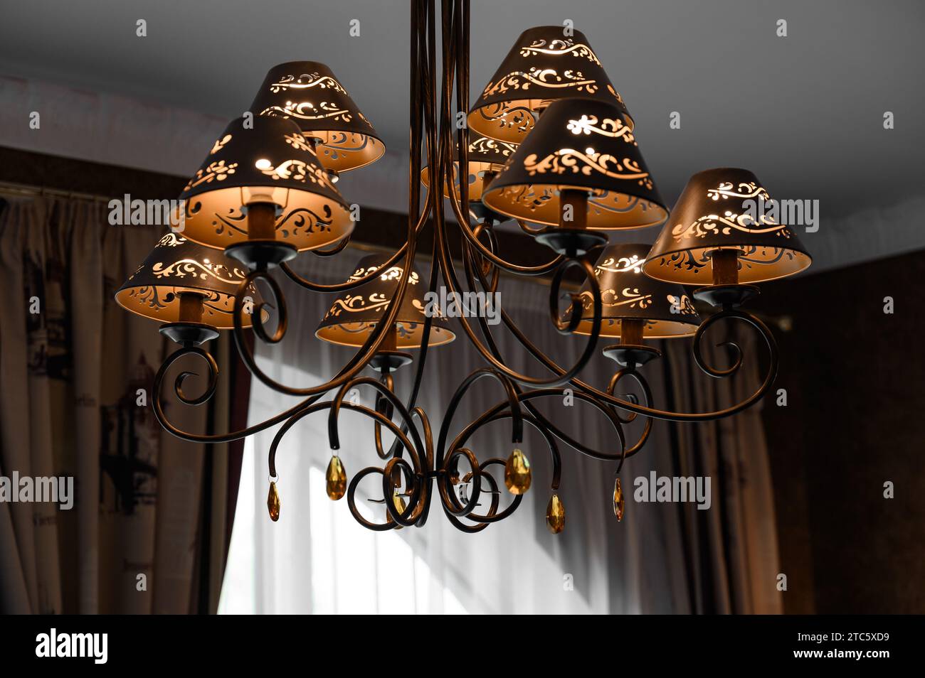 a chandelier with crystal elements and shades is attached and hangs from the ceiling. Stock Photo