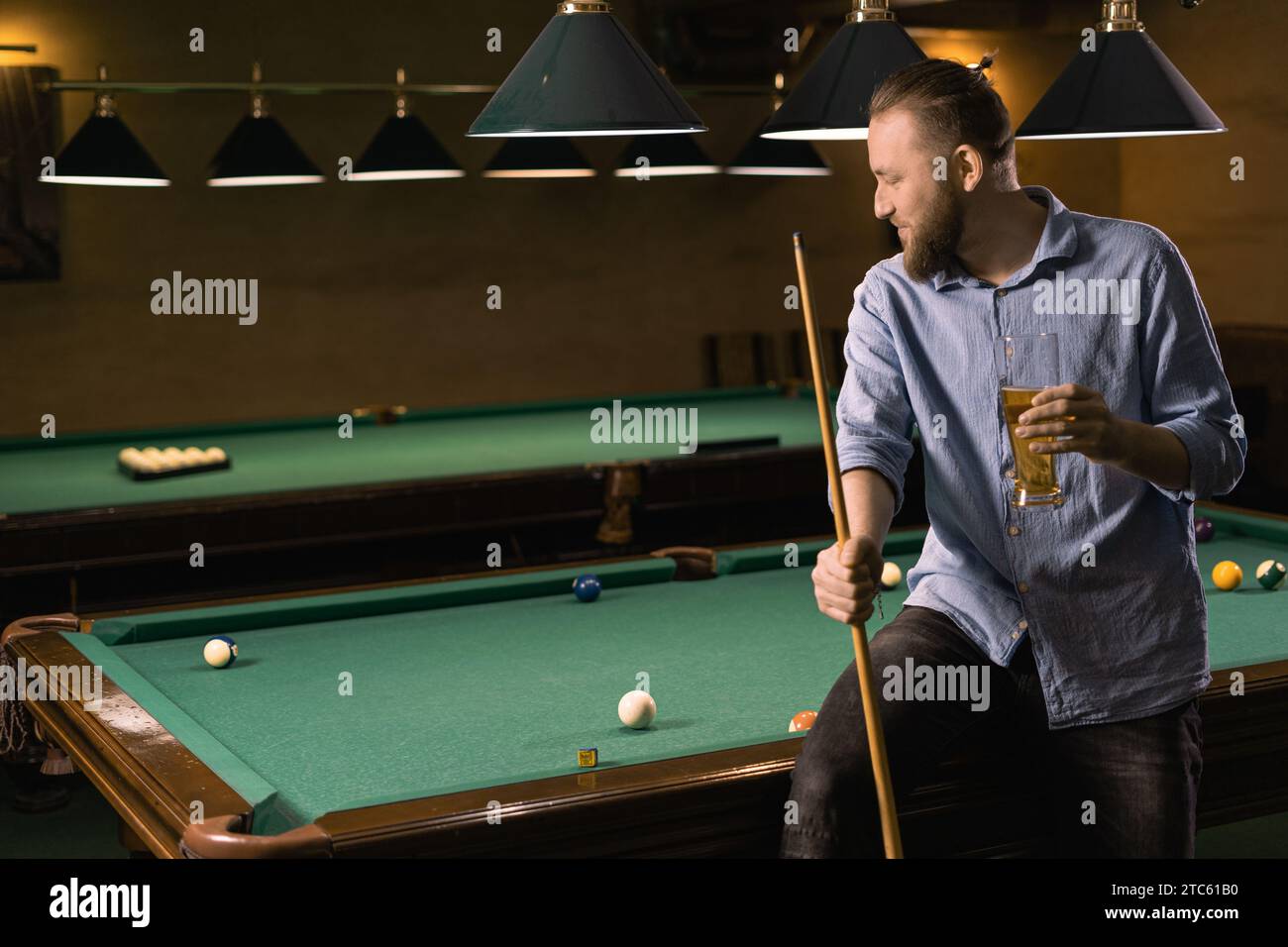 Billiard sport concept. Attractive man drinking beer near billiards