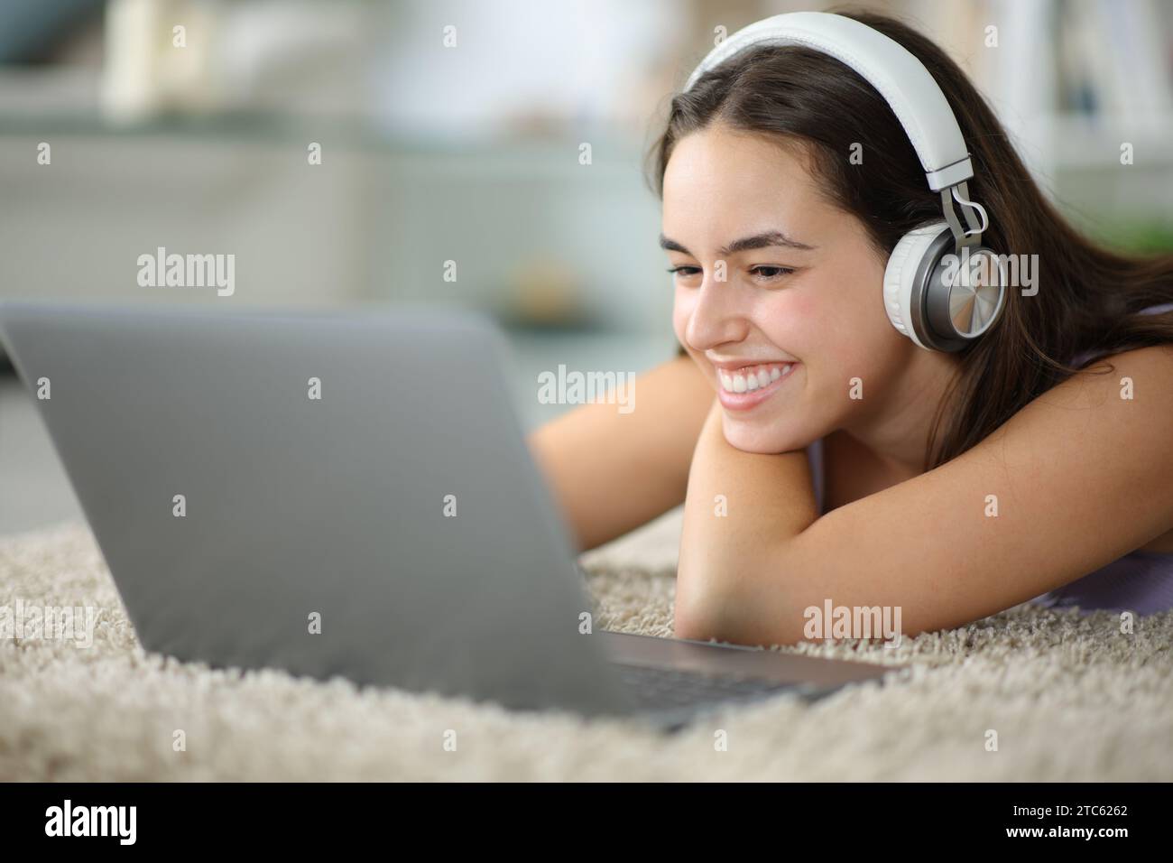 Happy woman with headphone checks laptop lying on the floor at home Stock Photo