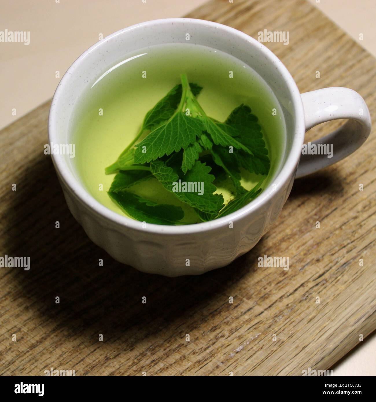 Hot mint tea in a white cup on a wooden desk closeup photo Stock Photo