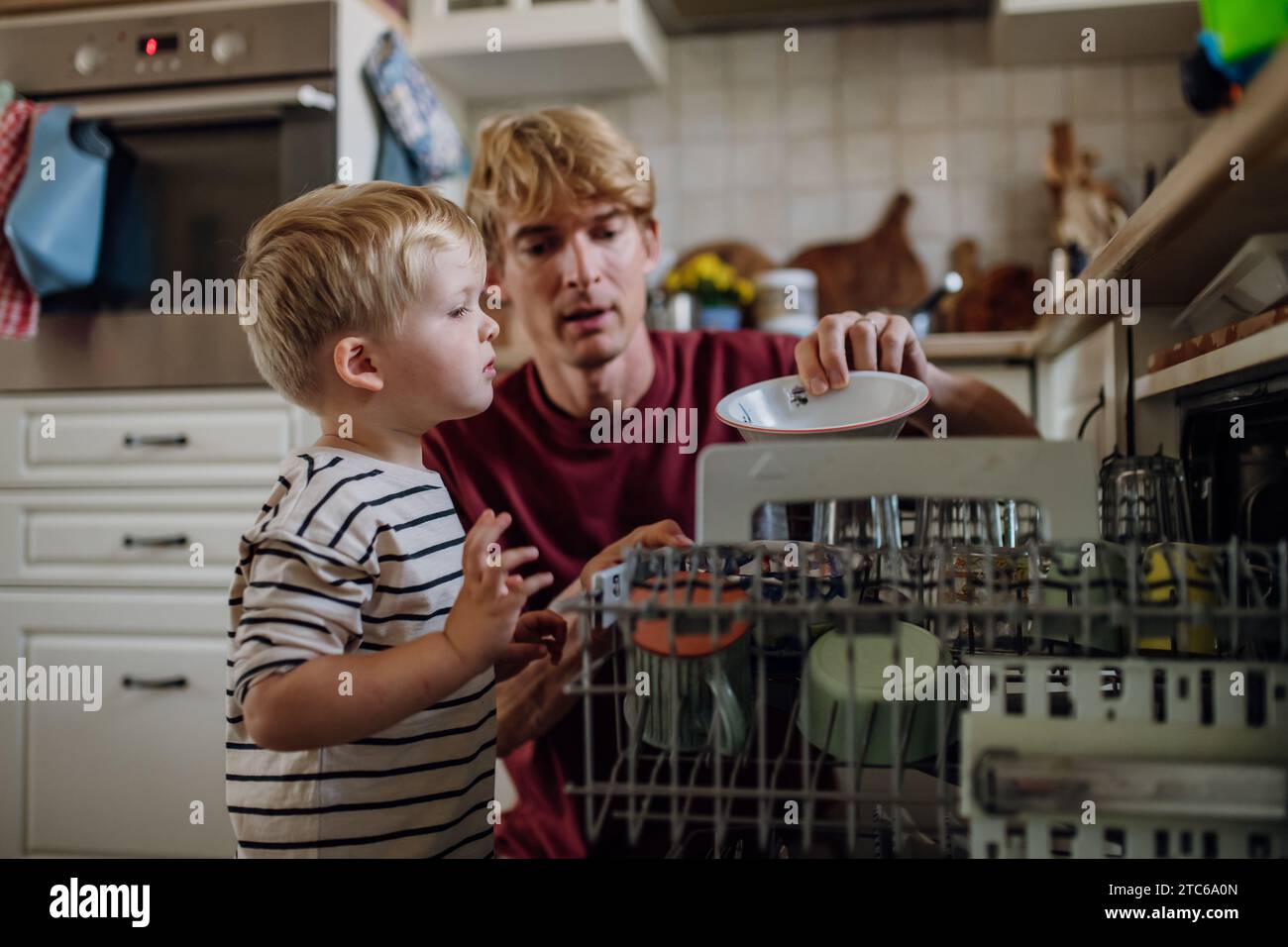 Little boy helping father to load dishwasher after breakfast. Cleaning