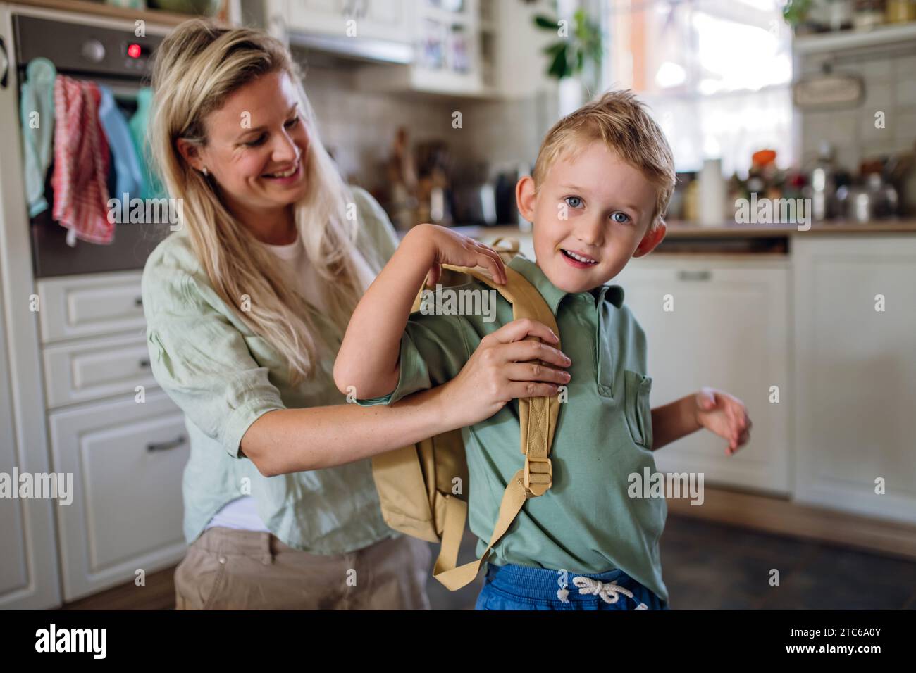 Mother saying goodbye to son before school, helping him to put backpack