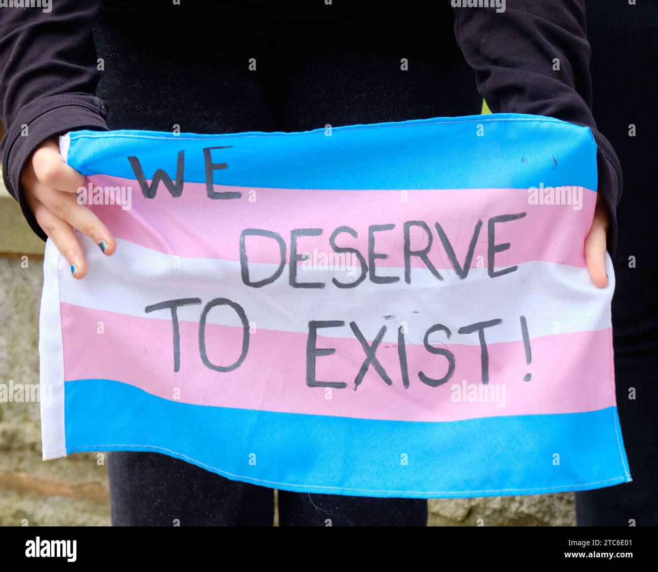 "We Deserve To Exist!" message written on Trans flag at rally Stock Photo