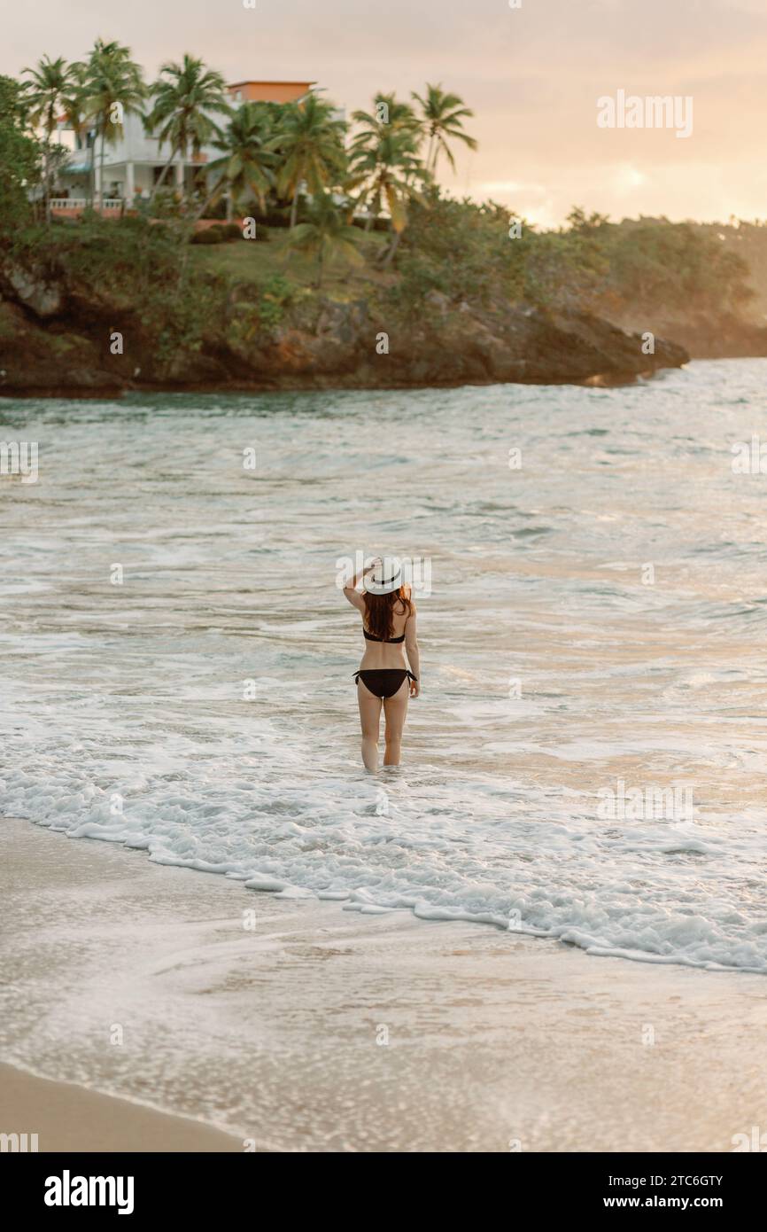 Young woman walking on Dominican beach at sunset, holding sun hat Stock ...