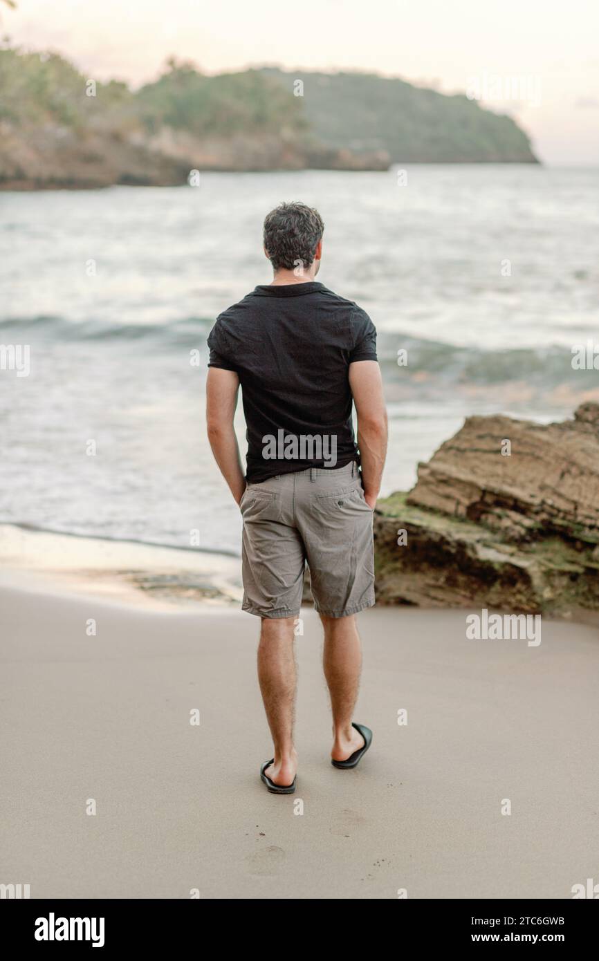 Man in thirties strolls coastal Dominican beach, serene view Stock Photo