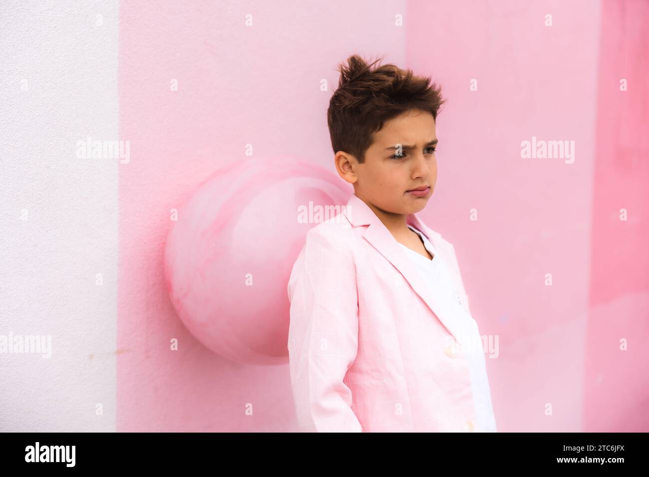Young boy leaning on a ball on the sidewalk in a suit all pink Stock Photo