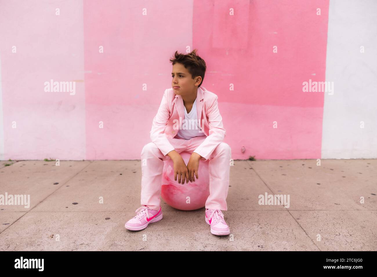 Photo young boy pondering on a ball on the sidewalk all pink Stock Photo