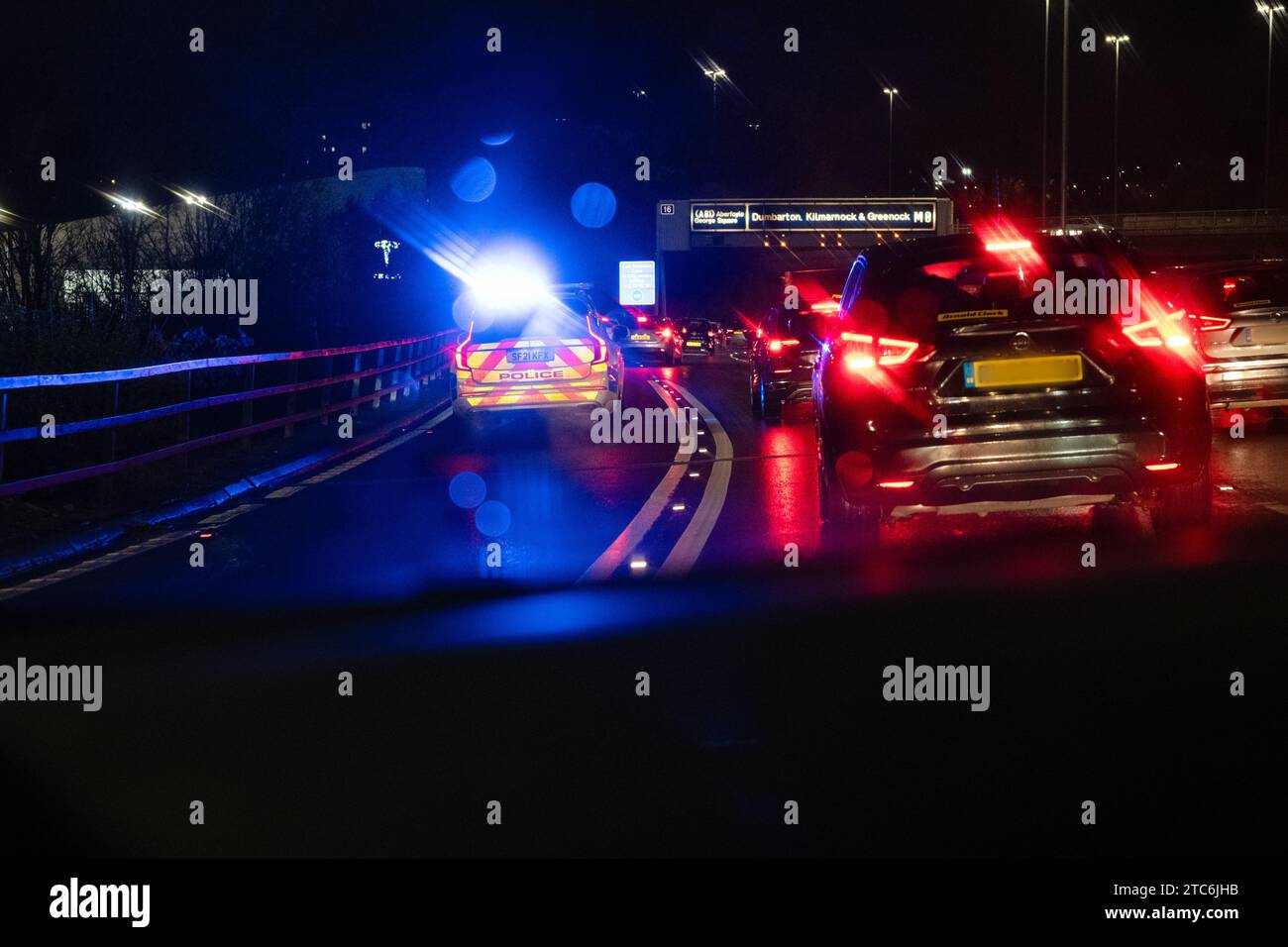 Police car with blue flashing lights at night responding to an emergency and joining heavy traffic on M8 motorway via junction 15 Glasgow Scotland, UK Stock Photo