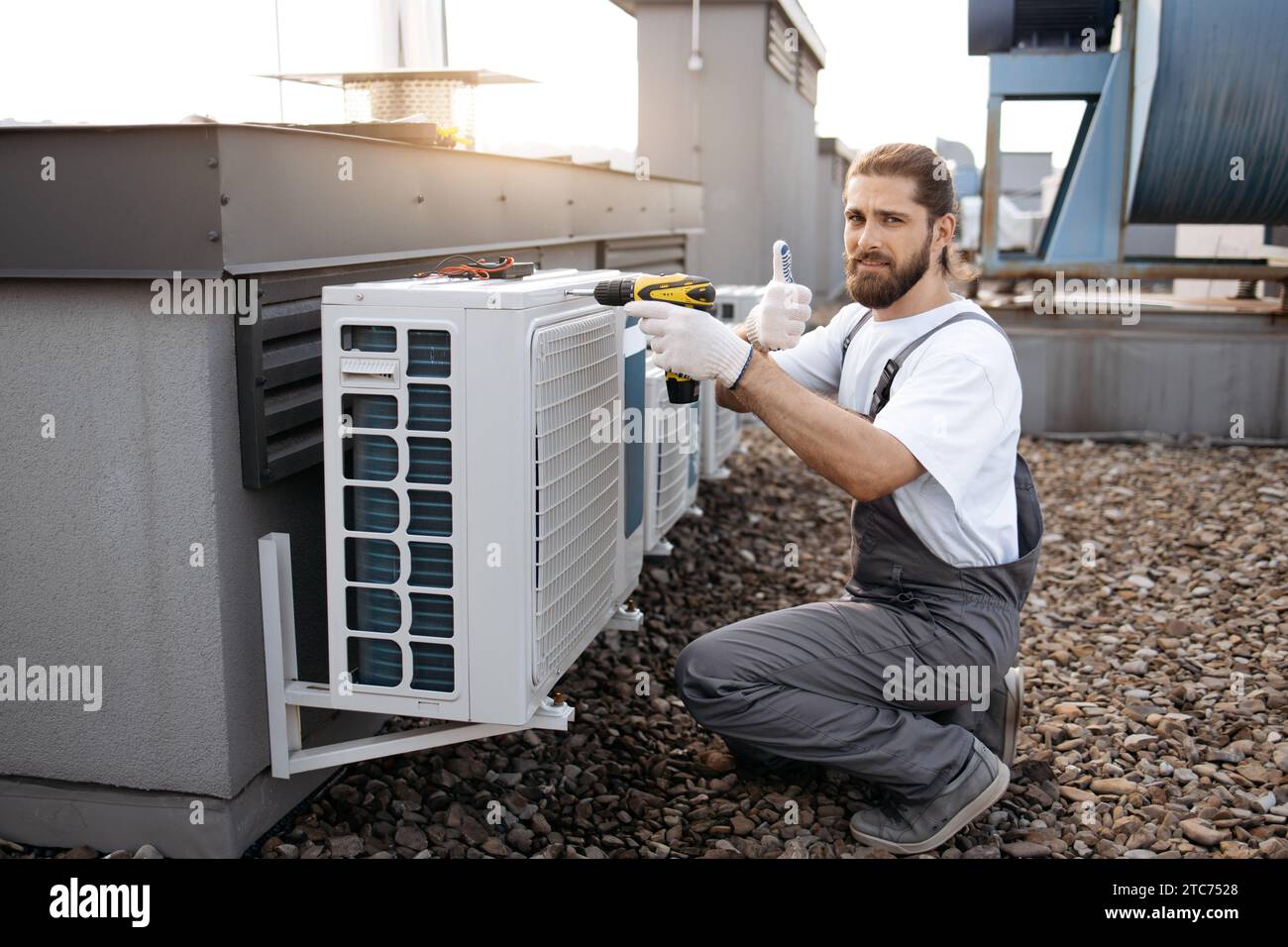 Male worker repairing conditioner while using drill outdoor Stock Photo