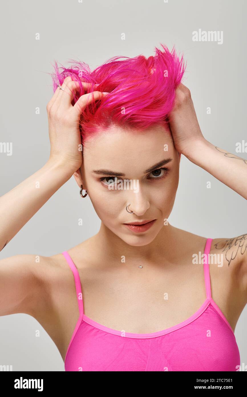 portrait of alluring young woman with pink hair and tattoos posing and touching her hair, fashion Stock Photo